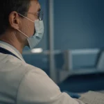 Ritratto di un medico specialista che esamina attentamente un'immagine ecografica della tiroide su uno schermo, espressione concentrata, luce soffusa da studio, profondità di campo ridotta, obiettivo prime 35mm, toni duotone blu e grigio.