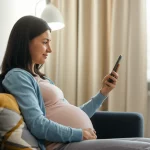 Fotografia stile reportage, una giovane donna incinta guarda con fiducia il suo smartphone mentre si rilassa a casa su un comodo divano, simboleggiando l'accesso alla cura prenatale digitale e il supporto ricevuto tramite telemedicina, obiettivo 50mm, luce soffusa del mattino che entra dalla finestra, profondità di campo media che mantiene a fuoco sia la donna che il contesto domestico, colori naturali e caldi, espressione serena.