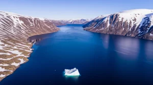 Veduta aerea di Nuup Kangerlua, un fiordo groenlandese, con acque blu scuro che si snodano tra montagne rocciose e parzialmente innevate. Un piccolo iceberg galleggia in primo piano. Obiettivo grandangolare 20mm, fotografia aerea, luce diurna brillante, messa a fuoco nitida sull'intero paesaggio.