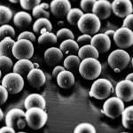 Immagine macro ad altissima risoluzione di particelle sferiche di catalizzatore BSCF su una superficie metallica lucida, illuminazione laterale controllata e drammatica per enfatizzare la tridimensionalità e la texture fine delle particelle, obiettivo macro 105mm, messa a fuoco precisa e selettiva, alta definizione.