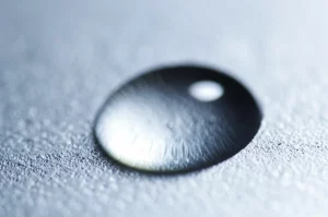 Primo piano macro di una goccia di gel di silice termoconduttivo trasparente su una superficie metallica di un componente elettronico, obiettivo macro 105mm, alta definizione, illuminazione laterale controllata per evidenziare la texture viscosa del gel.