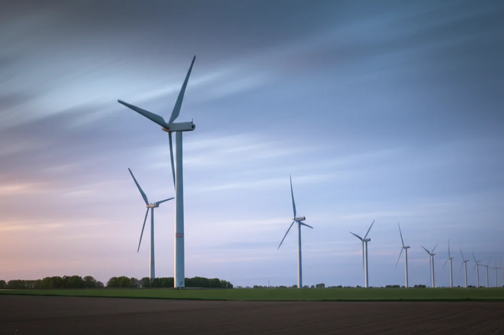 Turbine eoliche moderne che si stagliano contro un cielo danese al tramonto, simbolo di energia rinnovabile e impatto economico locale, fotografia paesaggistica, obiettivo grandangolare 20mm, lunga esposizione per nuvole soffici.