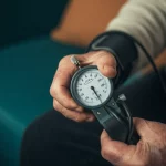 Mano di un paziente anziano che stringe un dinamometro medico per misurare la forza della presa, simbolo di fragilità e scompenso cardiaco. Prime lens, 35mm, depth of field, luce soffusa.