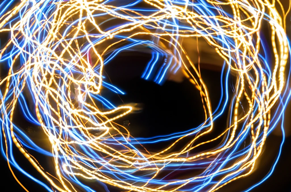 Visualizzazione astratta di onde sinusoidali luminose multiple e interconnesse su sfondo scuro, rappresentanti traiettorie di segni vitali previste dall'IA in terapia intensiva, fotografia wide-angle 15mm, lunga esposizione per scie luminose.