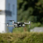 Immagine fotorealistica di un drone civile di medie dimensioni per ispezioni che sorvola silenziosamente un quartiere residenziale tedesco moderno e verdeggiante in una giornata di sole, vista leggermente dal basso con obiettivo zoom 35mm, messa a fuoco nitida sul drone, sfondo leggermente sfocato per profondità di campo.