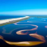 Vista aerea panoramica del sistema di laghi interconnessi di Kosi Bay, Sudafrica, al confine con l'Oceano Indiano. Si notano le diverse tonalità dell'acqua, da turchese vicino alla foce a più scuro verso l'interno, circondate da dune sabbiose coperte di vegetazione e foreste. Fotografia aerea con drone, lente grandangolare 18mm, luce solare del mattino, alta risoluzione, colori vividi.
