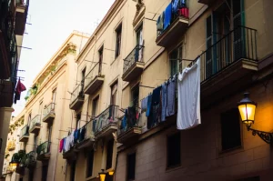 Veduta a livello strada di un edificio residenziale nel centro storico di Barcellona (Raval), obiettivo 35mm, luce naturale del tardo pomeriggio, focus sui balconi con panni stesi e facciate con segni del tempo, che suggerisce le diverse condizioni abitative al suo interno, profondità di campo media.