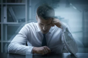 Un'immagine concettuale che rappresenta il presenteismo: una persona fisicamente presente in ufficio ma mentalmente assente o poco produttiva, magari con un effetto di trasparenza o sfocatura sulla figura rispetto all'ambiente circostante, obiettivo 35mm, profondità di campo, toni freddi.