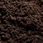 Fotografia macro di un campione di suolo fertile e scuro proveniente da una foresta giapponese, lente macro 100mm, alta definizione, illuminazione laterale controllata che evidenzia la struttura granulare e la presenza di materia organica, suggerendo la ricca vita microbica al suo interno.