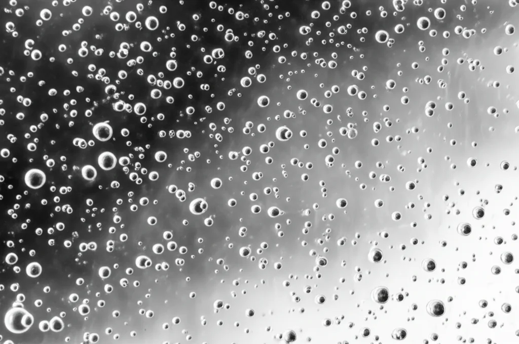Macro fotografia di una superficie in acciaio inox rivestita con resina epossidica trasparente antimicrobica contenente clorexidina, obiettivo macro 100mm, illuminazione controllata da studio, alta definizione, messa a fuoco precisa sulle micro-bolle o particelle sospese all'interno della resina indurita, mostrando la chiarezza del materiale.