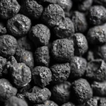Macro fotografia, lente 80mm, primo piano su particelle di biochar scuro e poroso derivato da gusci di arachidi nere, visibilmente modificate con particelle di ferro che conferiscono una leggera lucentezza, su sfondo neutro, illuminazione controllata da studio, alta definizione, focus preciso sulla texture.