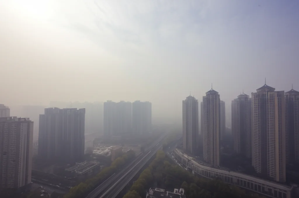 Immagine evocativa dell'impatto dell'inquinamento atmosferico sulla salute pubblica in Cina, con particolare riferimento all'ictus ischemico. Fotografia di un panorama urbano cinese con smog visibile, obiettivo grandangolare 18mm, lunga esposizione per catturare il movimento delle nuvole di smog, messa a fuoco nitida sull'orizzonte.