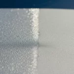 Immagine fotorealistica di un campione dell'idrogel ASPIRE che mostra la sua texture unica, metà esposta al sole diretto e metà all'ombra, con una leggera condensa visibile sulla superficie più fredda, obiettivo macro 70mm, luce diurna naturale, alta definizione, per rappresentare la tecnologia di raffreddamento passivo.