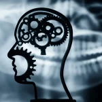 Fotografia concettuale, luce soffusa, un profilo stilizzato di una testa umana diviso a metà: una parte mostra ingranaggi cerebrali stilizzati, l'altra una radiografia dentale sfocata. Obiettivo 50mm, profondità di campo, toni blu e grigi duotone.