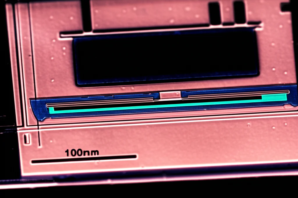 Primo piano macro, lente 100mm, di un dispositivo CMUT pre-caricato, mostrando i dettagli microfabbricati su substrato di vetro borosilicato. L'illuminazione è controllata per evidenziare le strutture interne complesse e la precisione della fabbricazione. Alta definizione e messa a fuoco precisa sull'area attiva del trasduttore.