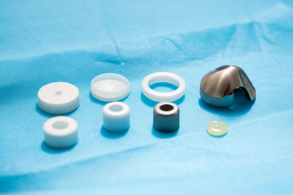 Fotografia still life di componenti di una protesi UKA a cuscinetto fisso (componente femorale, tibiale e diversi inserti di spessore variabile) disposti ordinatamente su un telo chirurgico sterile. Obiettivo macro 60mm, illuminazione controllata, alta definizione dei materiali metallici e plastici.