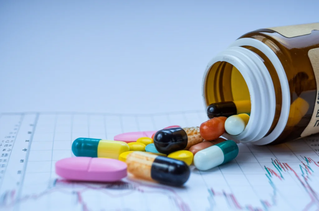 Immagine fotorealistica, obiettivo 35mm, profondità di campo, che mostra una collezione di diverse capsule e pillole di antibiotici che fuoriescono da una bottiglia da farmacia vintage su una superficie che mostra deboli grafici delle tendenze di consumo, simboleggiando la lunga storia e i complessi modelli dell'uso degli antibiotici.