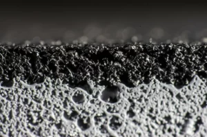 Primo piano macro di una sezione trasversale di asfalto modificato SBS dopo invecchiamento naturale in regione geliva, illuminazione controllata laterale per evidenziare la texture, obiettivo macro 100mm, alta definizione dei dettagli della microstruttura polimerica leggermente degradata e delle micro-aggregati, sfondo sfocato.