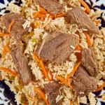 Un piatto complesso e tradizionale dell'Asia Centrale, forse Beshbarmak o Plov, fotografato dall'alto con un obiettivo macro 105mm. L'illuminazione è controllata, quasi da studio, per esaltare la texture della carne, del riso o della pasta e delle verdure. Alta definizione e messa a fuoco estremamente precisa sui singoli ingredienti.