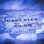 Immagine concettuale che mostra una doppia elica di DNA stilizzata e luminosa sovrapposta a una mappa sfocata della Spagna, con un focus particolare sulla regione di Castilla y León evidenziata. Illuminazione drammatica con toni blu e viola, stile cinematografico, lente 50mm, profondità di campo ridotta per enfatizzare il DNA.