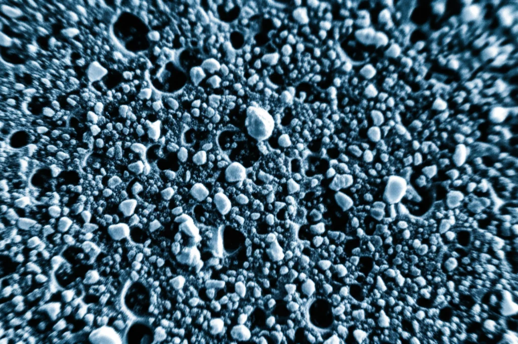 Immagine astratta e futuristica che rappresenta la microstruttura di un composito metallico avanzato AA7075/B4C/ZrO2, con particelle ceramiche (B4C, ZrO2) disperse in una matrice metallica (AA7075), colori high-tech blu metallico e grigio argento duotone, obiettivo macro 60mm, alta definizione, illuminazione drammatica controllata.