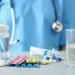 Immagine fotorealistica di una flebo di chemioterapia con cisplatino accanto a un bicchiere d'acqua e farmaci antiemetici su un tavolino medico, simbolo delle strategie di supporto, obiettivo macro 85mm, alta definizione, illuminazione controllata.