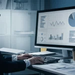 Immagine fotorealistica di un ufficio di un management accountant in un ospedale durante la pandemia, con grafici sullo schermo del computer e documenti sparsi sulla scrivania, luce tesa ma focalizzata, obiettivo 35mm, stile duotono seppia e blu scuro.