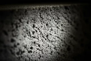 Immagine fotorealistica di un campione di calcestruzzo ad alta resistenza sezionato, illuminato per mostrare la sua struttura densa e compatta grazie ai nano-additivi, lente macro 100mm, alta definizione, illuminazione controllata che evidenzia le micro-particelle integrate.