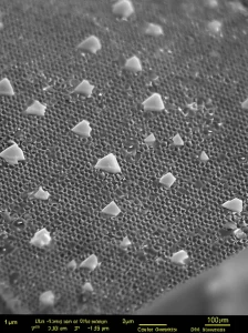 Macro fotografia, 100mm lens, high detail, controlled lighting, che mostra la struttura intricata di un cristallo fotonico rivestito di TiO2, parzialmente coperto da un idrogel trasparente contenente enzimi. La luce si riflette in modo selettivo dalla superficie nanostrutturata, evidenziando il concetto di biosensore ottico ibrido.