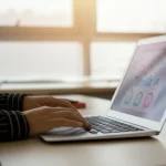 Fotografia di un'aula universitaria moderna e luminosa, focalizzata su un laptop aperto su una piattaforma di apprendimento musicale online. Sullo schermo, si intravede un'interfaccia utente con grafici di valutazione stilizzati e icone musicali. In primo piano, sfocata, una mano che interagisce delicatamente con il touchpad. Obiettivo prime 35mm, profondità di campo ridotta per mettere a fuoco il laptop, illuminazione controllata che mescola luce naturale dalla finestra e luce artificiale calda, creando un ambiente accogliente e tecnologico.