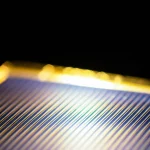 Primo piano fotorealistico di una cella solare a perovskite flessibile e semitrasparente, illuminata da una luce solare brillante ma controllata. Macro lens 100mm, high detail sulla struttura cristallina visibile attraverso gli strati sottili, luce naturale che ne esalta l'efficienza e la tecnologia avanzata.