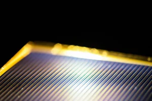 Primo piano fotorealistico di una cella solare a perovskite flessibile e semitrasparente, illuminata da una luce solare brillante ma controllata. Macro lens 100mm, high detail sulla struttura cristallina visibile attraverso gli strati sottili, luce naturale che ne esalta l'efficienza e la tecnologia avanzata.