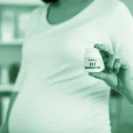Fotografia stile ritratto, 35mm lens, di una donna incinta sorridente che tiene in mano un integratore di vitamina B12 o un alimento ricco di B12 (es. uovo sodo), con uno sfondo leggermente sfocato che suggerisce un ambiente sano e luminoso, depth of field, duotone verde e bianco per un look fresco e salutare.