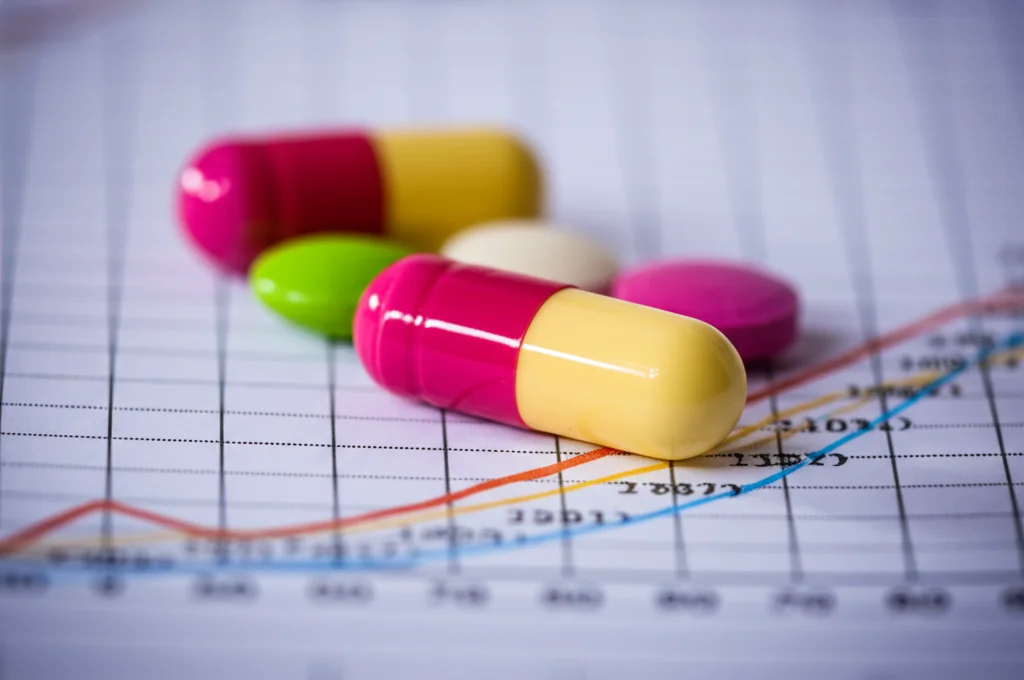 Primo piano di diverse pillole colorate per la terapia antiretrovirale (ART) contro l'HIV, disposte su un grafico astratto che mostra curve di efficacia e costi. Luce da studio controllata, obiettivo macro 100mm, alta definizione, messa a fuoco precisa sui dettagli delle pillole.