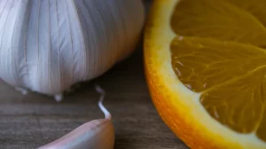 Primo piano macro di uno spicchio d'aglio fresco e una fetta d'arancia vibrante affiancati su una superficie di legno rustico, illuminazione controllata e morbida, alta definizione, lente macro 90mm, a simboleggiare l'unione protettiva di allicina ed esperidina per la fertilità maschile contro le tossine ambientali.