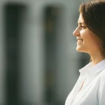 Ritratto fotografico di profilo di una donna sorridente che guarda verso la luce, simbolo di speranza dopo un percorso oncologico. Obiettivo 50mm, luce naturale morbida, sfondo leggermente sfocato, colori naturali e caldi.