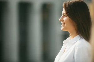 Ritratto fotografico di profilo di una donna sorridente che guarda verso la luce, simbolo di speranza dopo un percorso oncologico. Obiettivo 50mm, luce naturale morbida, sfondo leggermente sfocato, colori naturali e caldi.