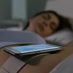 Smartphone posizionato sull'addome di una persona che dorme a letto, assicurato da una fascia. Luce notturna soffusa, focus sul dispositivo e sulla sua posizione. Obiettivo prime 35mm, profondità di campo per isolare il soggetto.