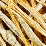 Primo piano estremo di fibre di cellulosa antiche e ingiallite, con dettagli microscopici visibili. Obiettivo macro 105mm, alta definizione, illuminazione laterale controllata per accentuare la texture e le variazioni di colore dal bianco sporco al giallo intenso.
