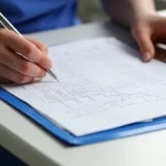 Fotografia realistica di mani di infermiere che compilano meticolosamente una cartella clinica cartacea su una scrivania in ospedale, luce focalizzata sul documento, obiettivo macro 60mm, alta definizione dei dettagli della scrittura e della texture della carta.