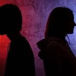 Immagine concettuale che mostra due silhouette di adolescenti, un ragazzo e una ragazza, su uno sfondo diviso a metà con colori e texture differenti (uno più caotico, l'altro più introspettivo), a simboleggiare le diverse influenze e percorsi di genere. Fotografia stile ritratto, obiettivo 50mm, profondità di campo media, illuminazione laterale per creare contrasto.
