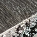 Primo piano fotorealistico di un pezzo di ferro-cromo con inclusioni di silicio, illuminato lateralmente per evidenziare la sua struttura metallica complessa e le diverse sfumature. Obiettivo macro 90mm, alta definizione, messa a fuoco selettiva sulla superficie texturizzata.