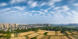 Veduta aerea grandangolare (10mm) di un paesaggio cinese che mostra la transizione tra una zona urbana densa e una rurale agricola sotto un cielo parzialmente nuvoloso, simboleggiando i cambiamenti climatici e l'impatto umano, long exposure per nuvole fluide.