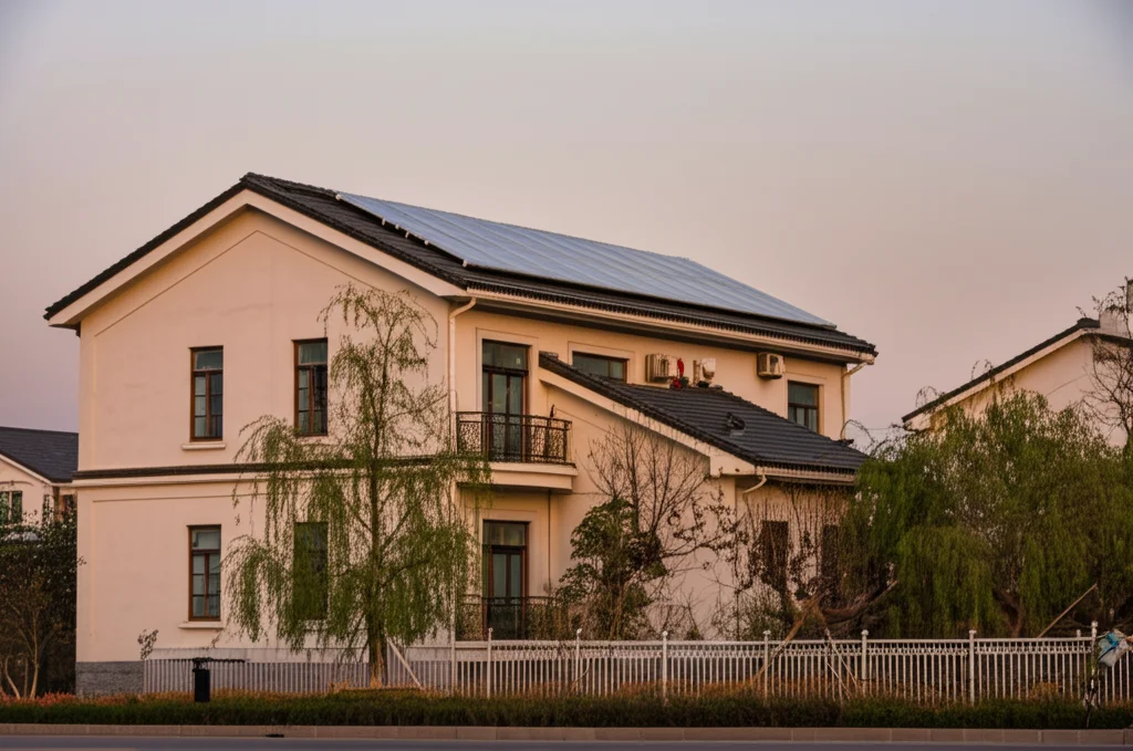 Immagine fotorealistica di una tipica abitazione suburbana nella provincia di Jiangsu, Cina, con pannelli solari sul tetto e un piccolo giardino curato, illuminata dalla luce calda del tramonto. Fotografia architettonica, obiettivo 24mm, luce dorata, alta risoluzione, dettagli nitidi sull'edificio e sulla vegetazione circostante.