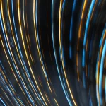 Visualizzazione astratta di traiettorie luminose curve nello spaziotempo, che interagiscono con superfici geometriche complesse rappresentanti condizioni al contorno non standard. Effetti di lente gravitazionale suggeriti. Obiettivo grandangolare, 15mm, lunga esposizione per scie luminose, messa a fuoco nitida sulle superfici.