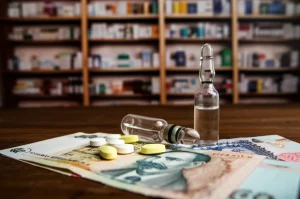 Macro Lens Shot, 85 mm, concentrandosi su alcune pillole ciprofloxacina e un'ampoula di gentamicina accanto alle note di valuta afghani su un bancone di farmacia in legno consumato a Kabul. Lucile controllate e leggermente drammatiche di evidenziazione delle trame, profondità di campo superficiale che sfoca gli scaffali della farmacia di fondo.