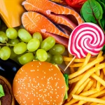 Una composizione artistica che contrappone cibi sani (frutta colorata, verdure a foglia verde, pesce azzurro) a cibi processati (hamburger, patatine fritte, dolci confezionati), simboleggiando la scelta dietetica nella gestione della FMF, fotografata con un obiettivo macro da 90mm, illuminazione drammatica e controllata per enfatizzare il contrasto, alta definizione dei dettagli.