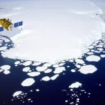 Immagine fotorealistica di un satellite altimetrico in orbita terrestre, visto da una prospettiva leggermente superiore, che sorvola la regione antartica. Sotto il satellite, si vede la calotta di ghiaccio bianca e frastagliata dell'Antartide che incontra l'oceano blu scuro, parzialmente coperto da banchisa fratturata. Il satellite emette un fascio radar (stilizzato) verso la superficie oceanica. Obiettivo zoom 35mm, profondità di campo che mantiene a fuoco sia il satellite che la superficie terrestre, luce solare nitida.