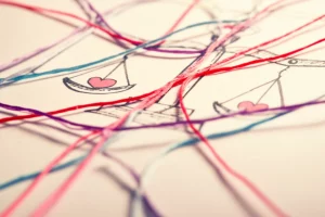 Fotografia simbolica astratta che rappresenta la complessità etica delle cure affermative di genere: un intreccio di fili colorati (simbolo dei diversi percorsi e identità) che attraversano una superficie medica stilizzata con simboli di bilance (giustizia) e cuori (cura), obiettivo 50mm, profondità di campo media, illuminazione diffusa e morbida, toni pastello caldi e freddi mescolati.