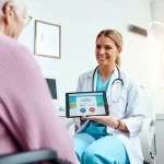 Fotografia realistica in stile reportage: una professionista sanitaria sorridente (donna, circa 40 anni, camice bianco) mostra un tablet con un'interfaccia web colorata e accessibile (il decision aid BESTa) a una paziente anziana (donna, circa 70 anni) seduta di fronte a lei in un ambulatorio medico luminoso e accogliente. Obiettivo 50mm, profondità di campo media che mantiene entrambi i soggetti a fuoco.